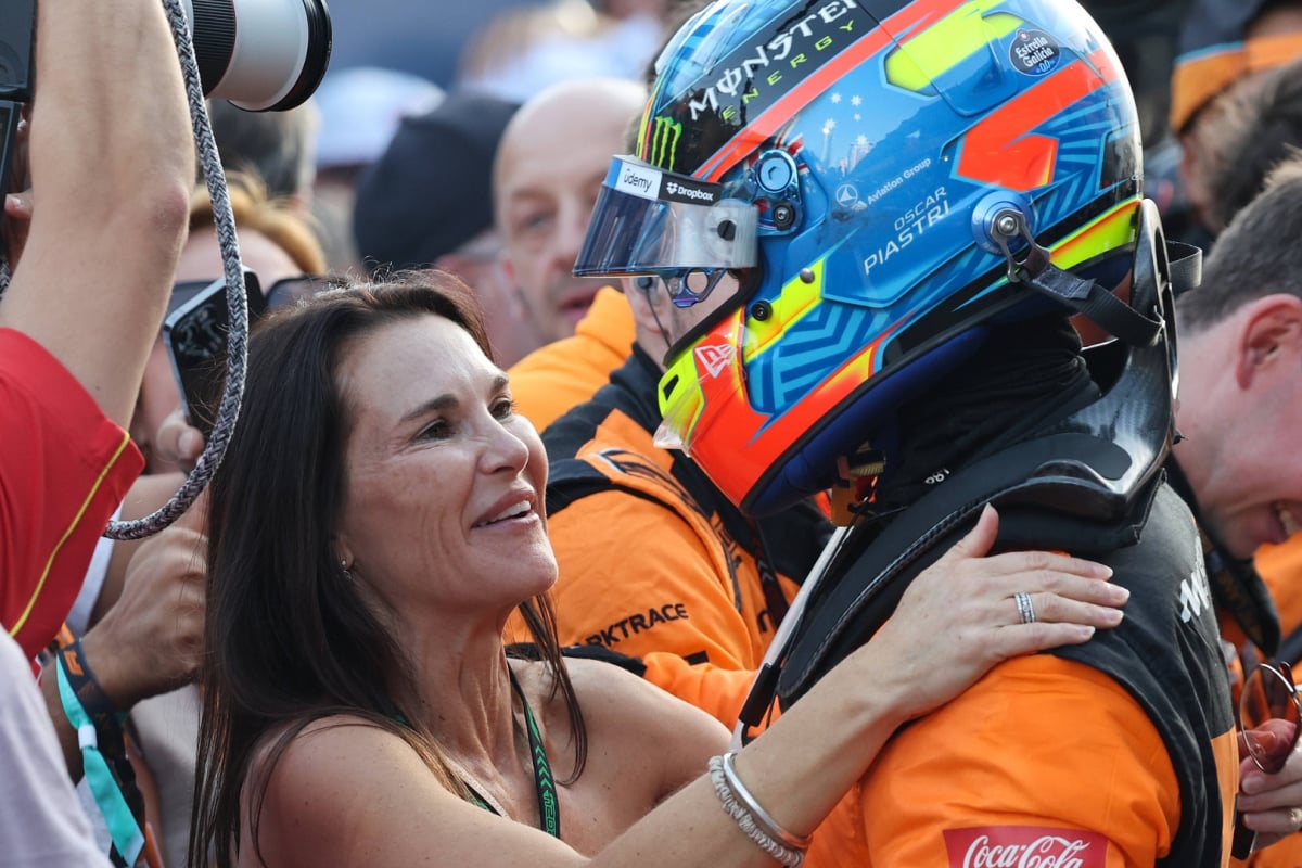 Nicole Piastri with her hands on her son's shoulders, Oscar has kept his race helmet on and is wearing a McLaren F1 race suit