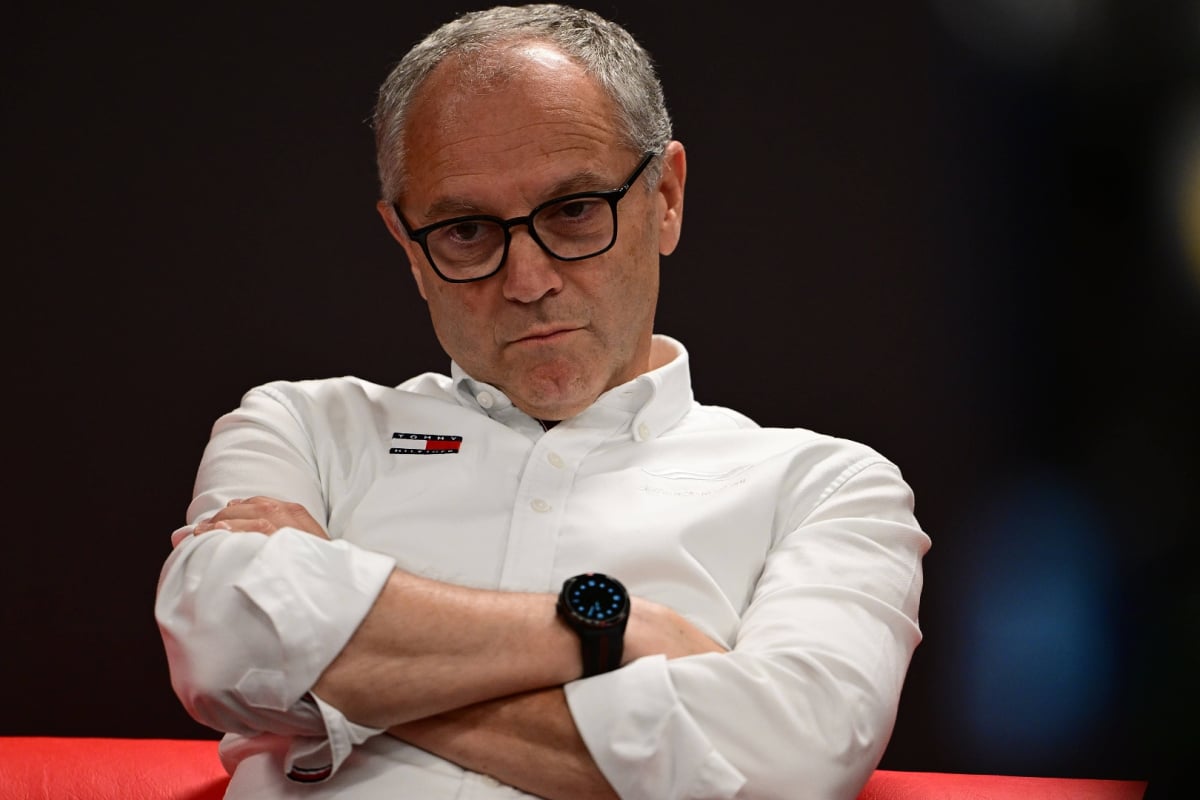 F1 president Domenicali sat with his arms crossed in a white shirt with Tommy Hilfiger logo, straight expression on his face