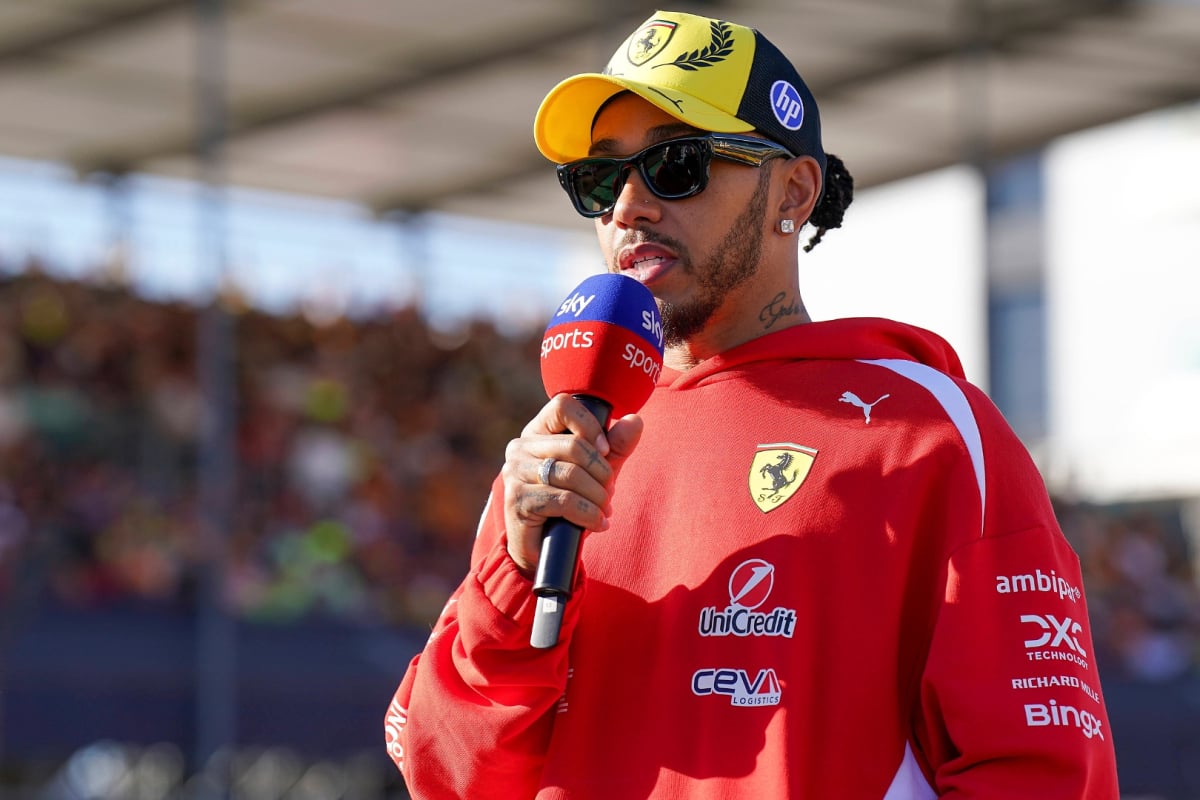 Hamilton in red Ferrari hoodie and yellow 2026 British GP cap holding Sky Sports F1 mic