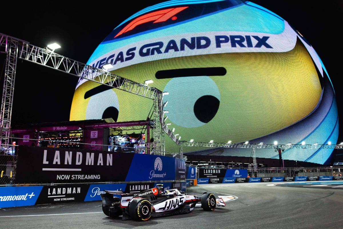 Ollie Bearman driving a Haas F1 car on the Vegas circuit beneath the smiling vegas GP helmet sphere