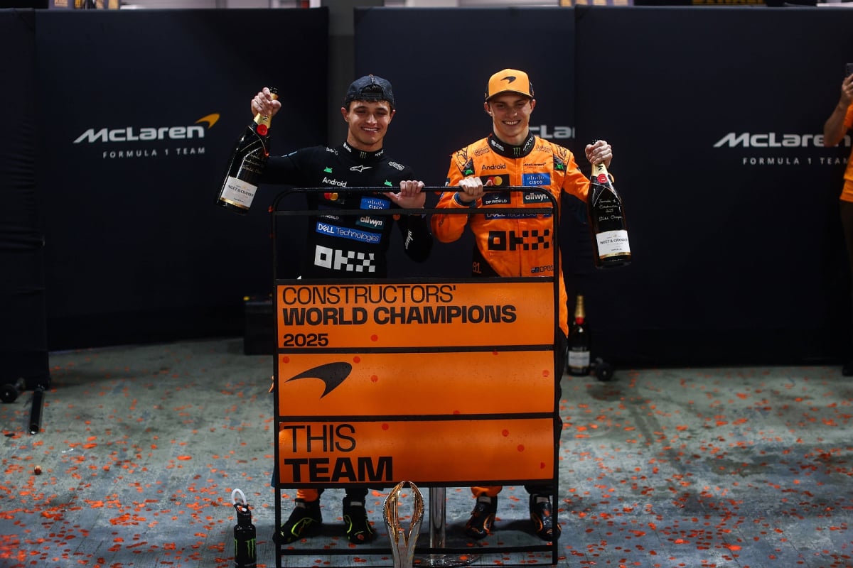 Norris and Piastri smiling in front of 'world champions' sign after the 2025 Singapore GP