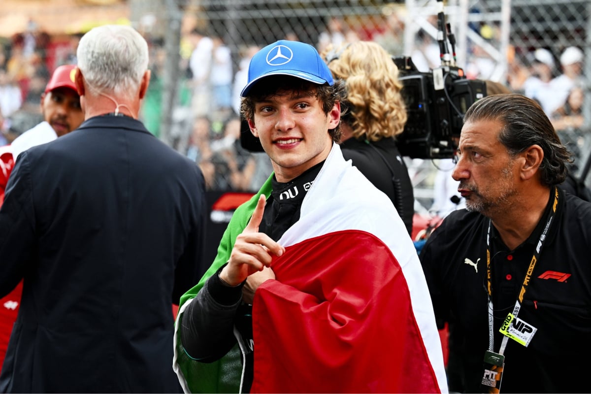 Antonelli with Italian flag wrapped around him in Mercedes race suit holding up one finger to demonstrate race win at Monaco GP