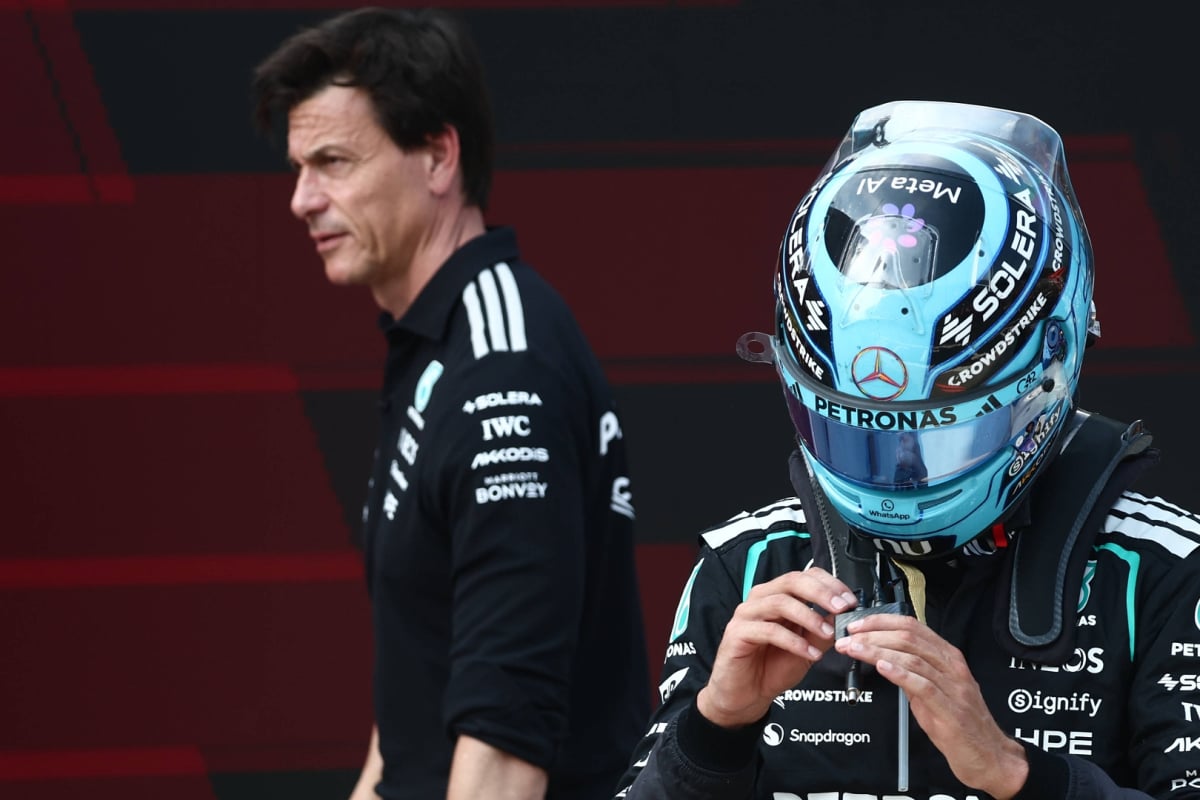 Russell in turquoise F1 helmet with Wolff walking past in the background looking serious