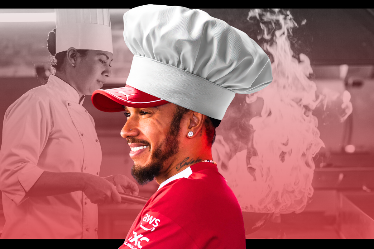 Lewis Hamilton smiling with a chef's hat on in full Ferrari gear, while chefs work tirelessly behind him with pans that have flames coming out from them