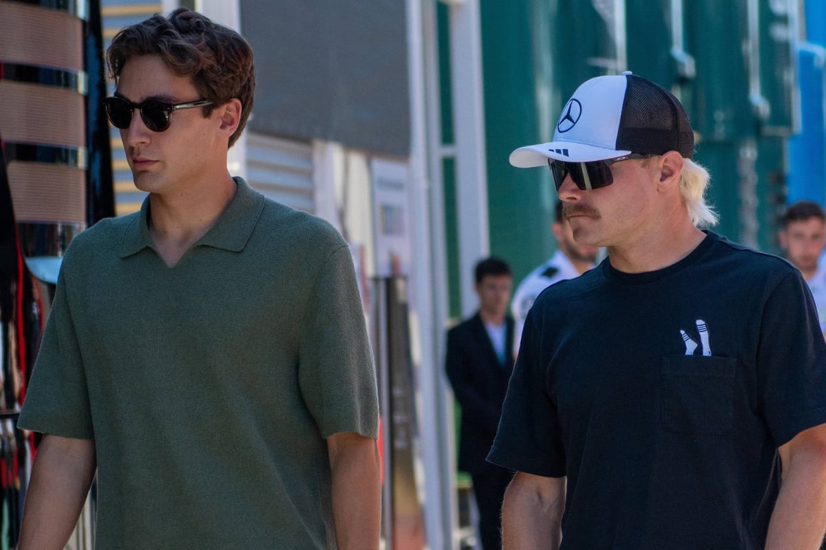 Russell in plain clothes walking through F1 paddock with Bottas in Mercedes hat