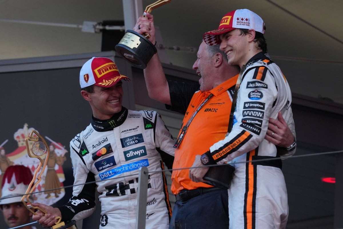 Norris and Brown holding trophies beaming at one another with Piastri joining them on the podium, smiling