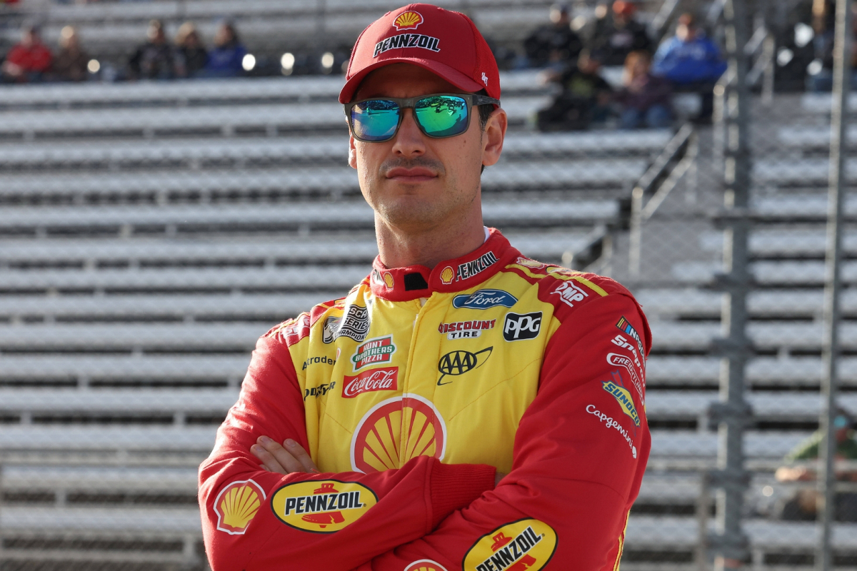An image of Team Penske NASCAR driver Joey Logano with his arms crossed on pit road