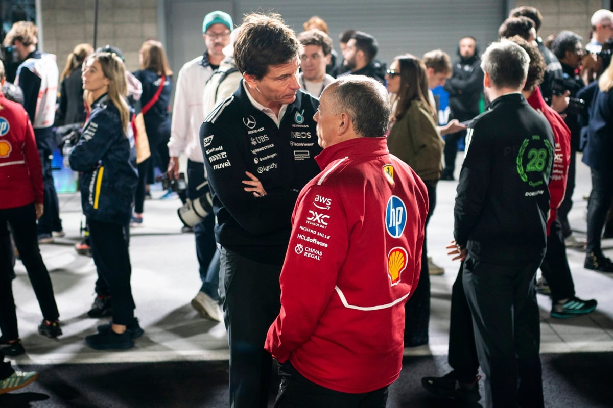 Wolff stood in conversation looking down on Vasseur at F1 track, wearing black Mercedes kit and red Ferrari jacket respectively