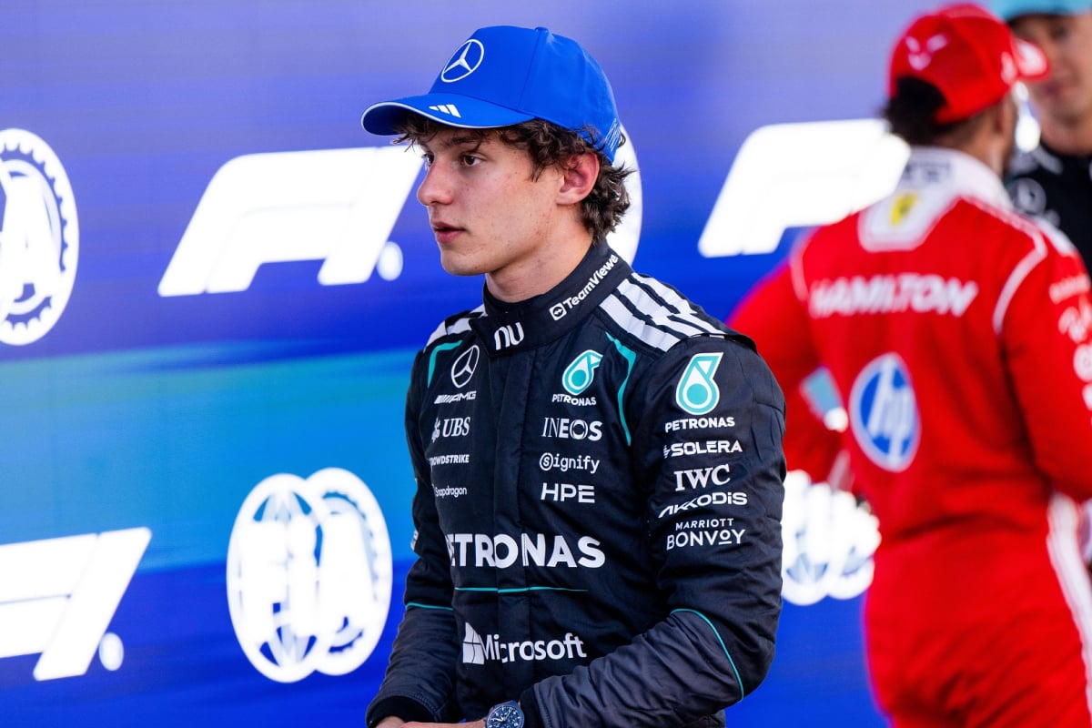 Antonelli in focus with F1 and FIA blue and white backdrop, Hamilton with his back to camera talking to Russell out of focus in shot