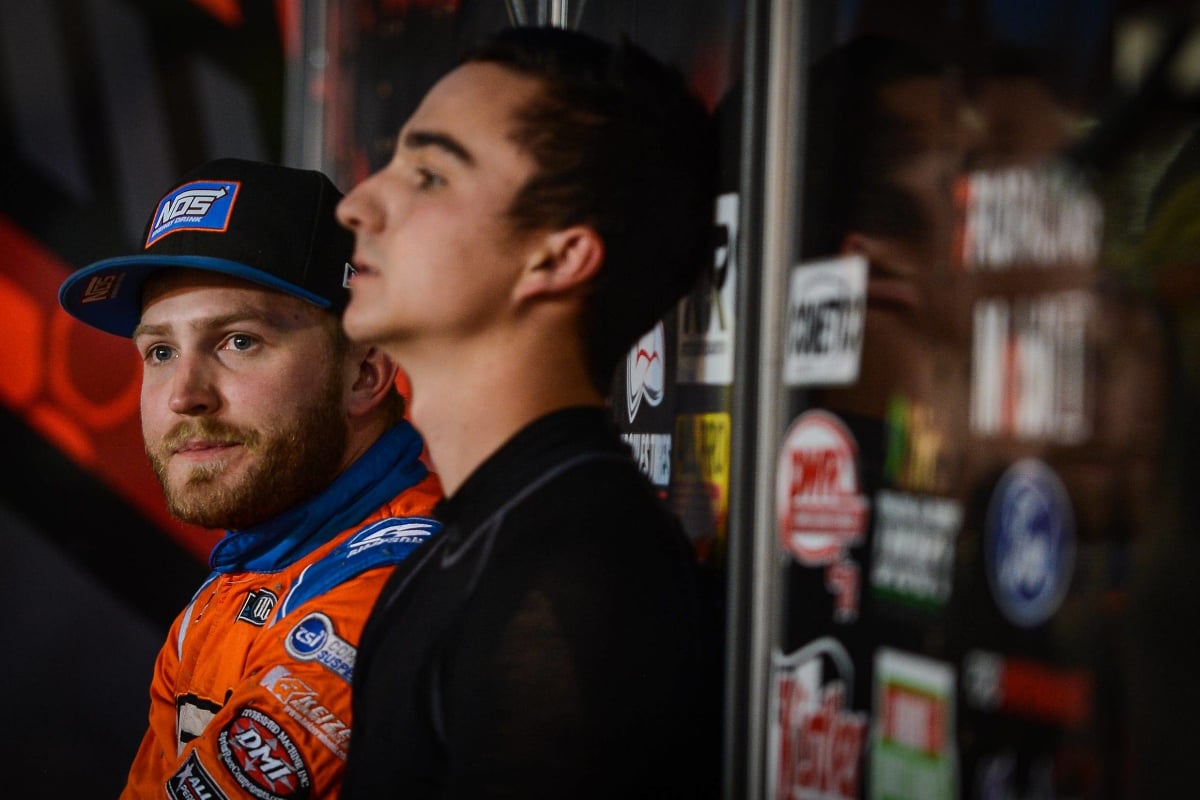 Tyler Courtney looks into the distance wearing a blue hat and orange race suit