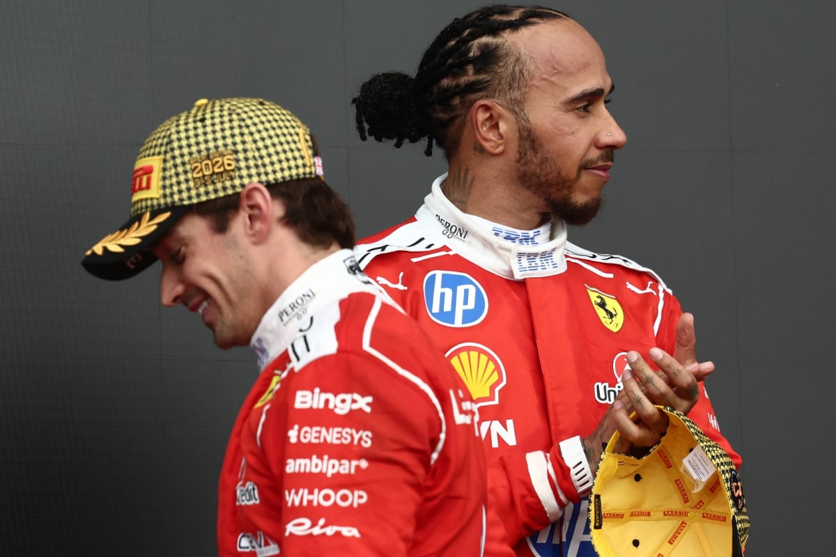 Leclerc's side profile in yellow and black Pirelli podium cap walking past Hamilton who is smiling and clapping