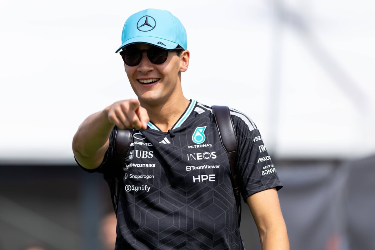 Russell laughing in Mercedes tee and cap pointing at the camera