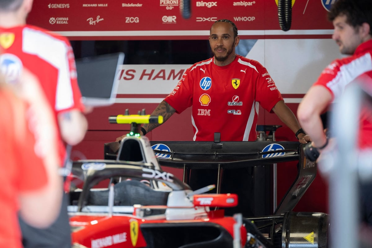 Hamilton stood over his Ferrari F1 car in the garage, smiling