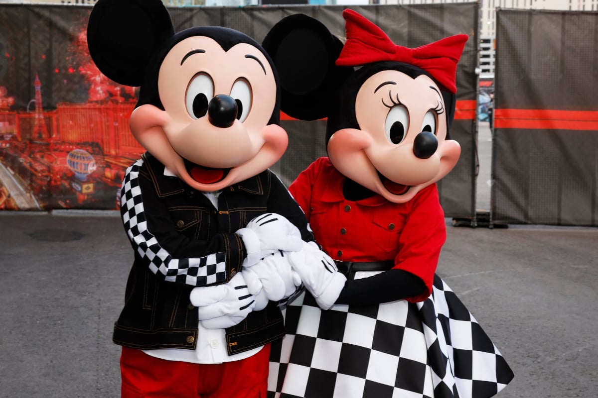 Lifesize Mickey and Minnie Mouse characters facing the camera holding hands in the F1 Las Vegas GP paddock.
