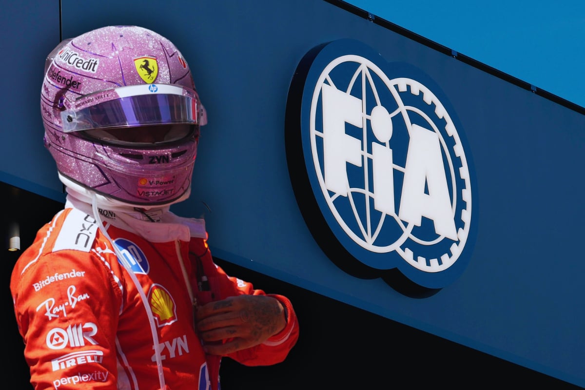Hamilton in pink F1 helmet in Ferrari race suit with white FIA logo on a blue building in the background
