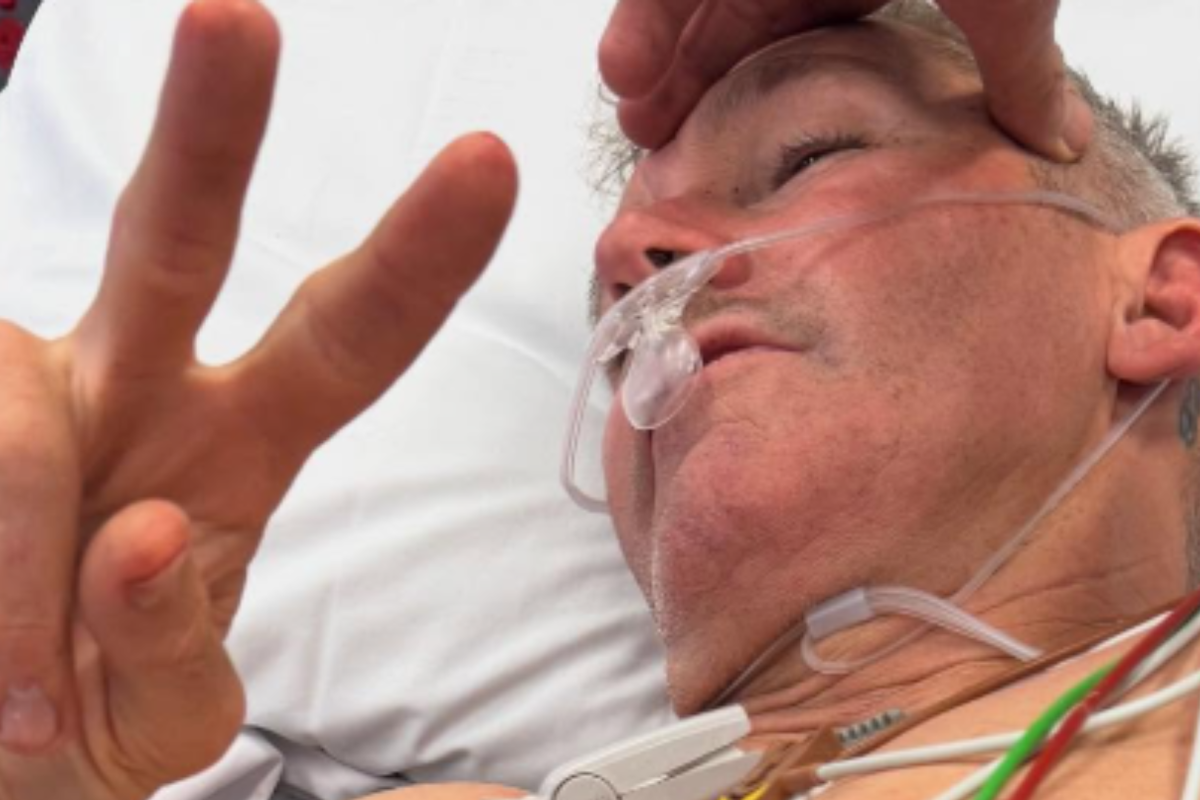 A severely injured Troy Bayliss gives a peace gesture to show he is ok after being taken in by an ambulance