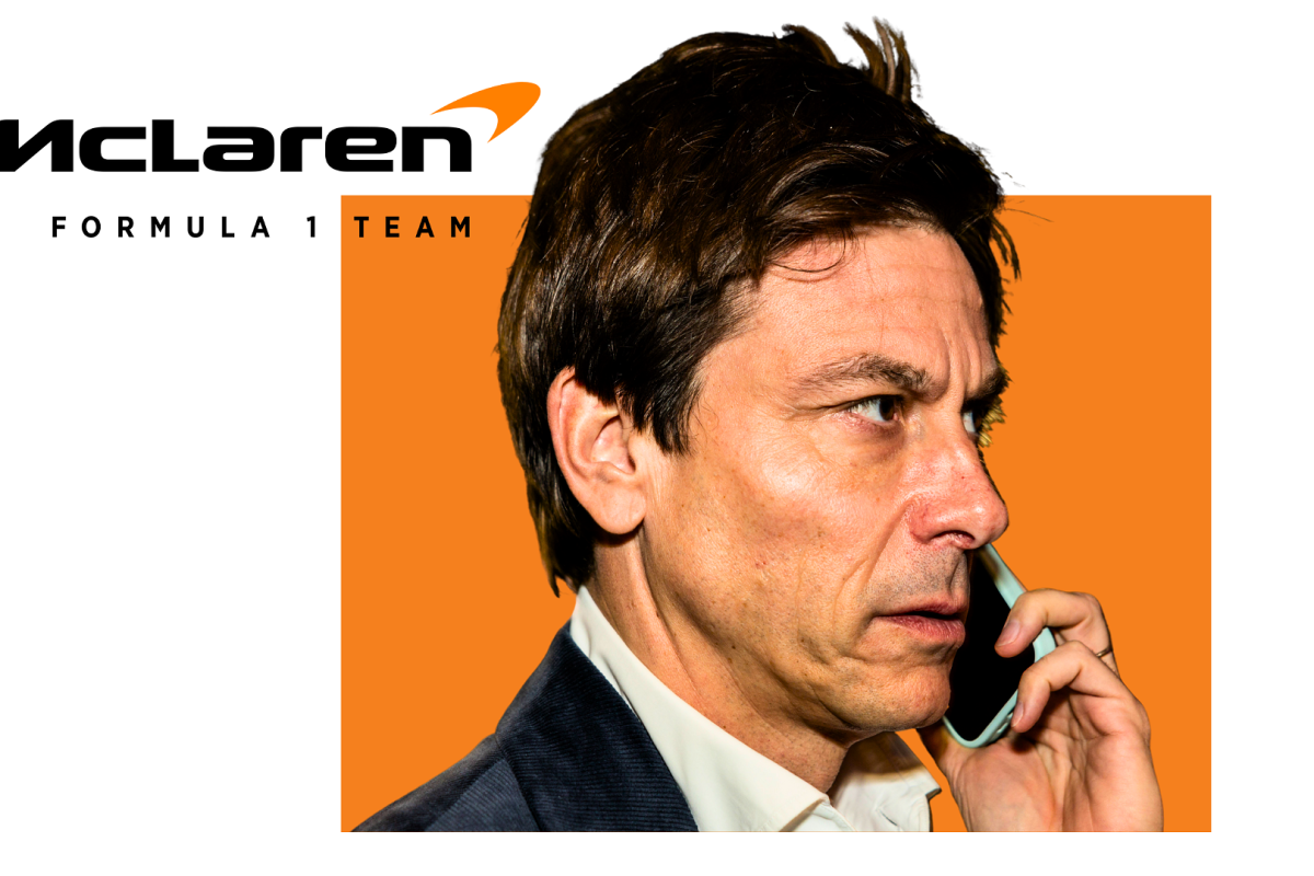 Toto Wolff talks on a phone in front of a McLaren background