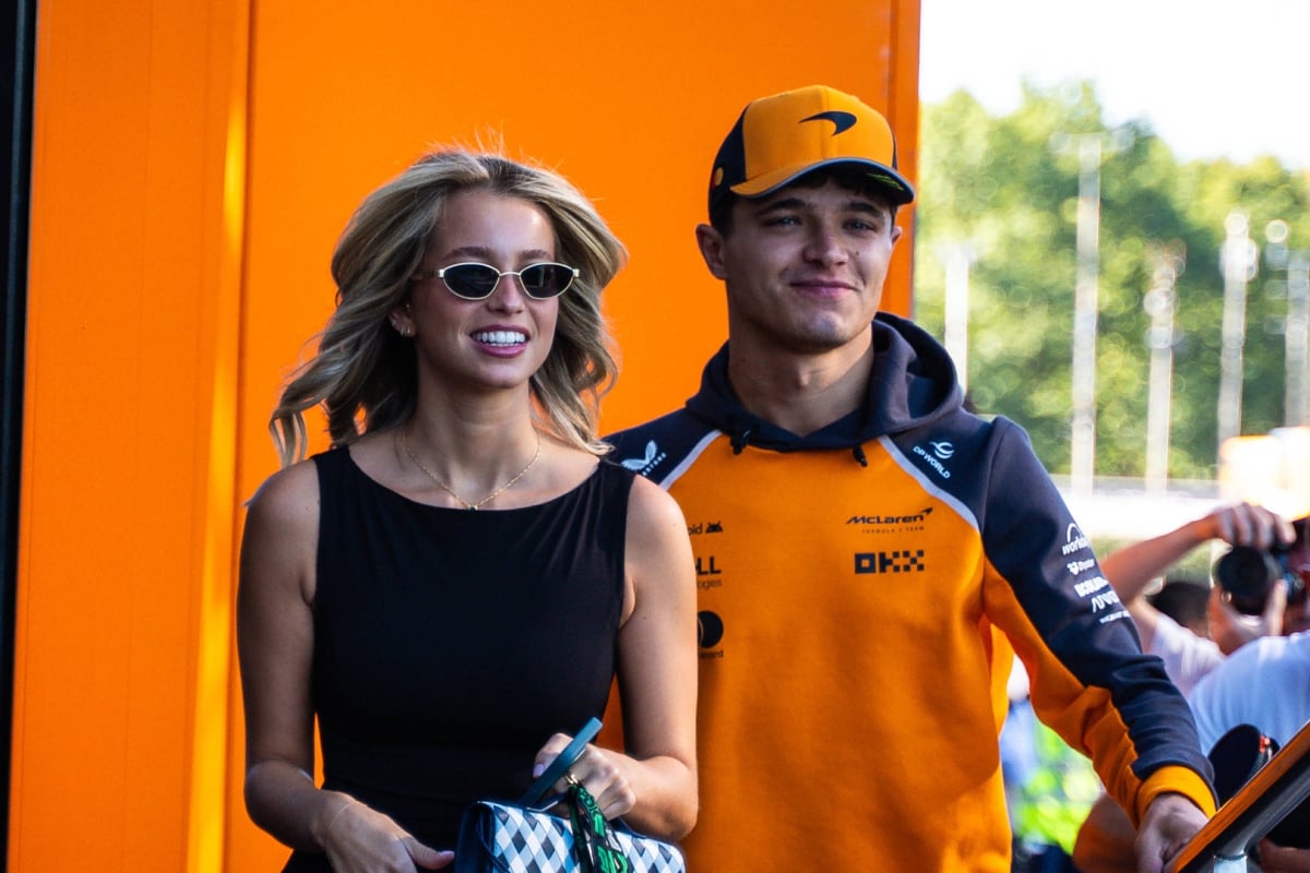 Norris and his girlfriend smiling as they walk into the McLaren motorhome in an F1 paddock