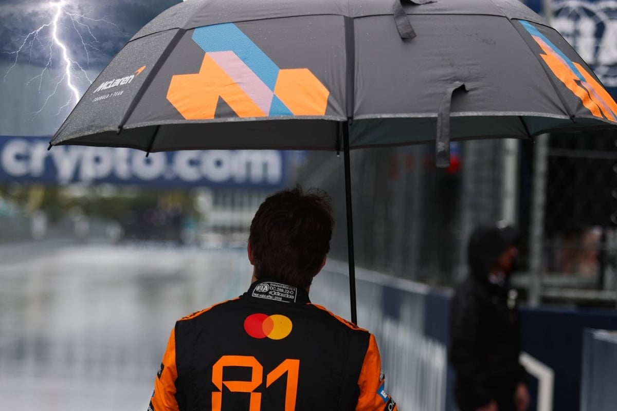 Oscar Piastri holds an umbrella as a superimposed lightning bolt hits his umbrella at the Miami GP