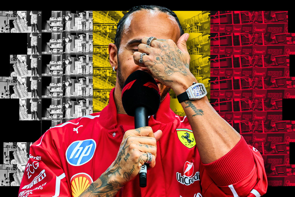 Hamilton in red Ferrari jacket holding F1 mic with hand on his face in front of black, yellow and red Belgian flag background