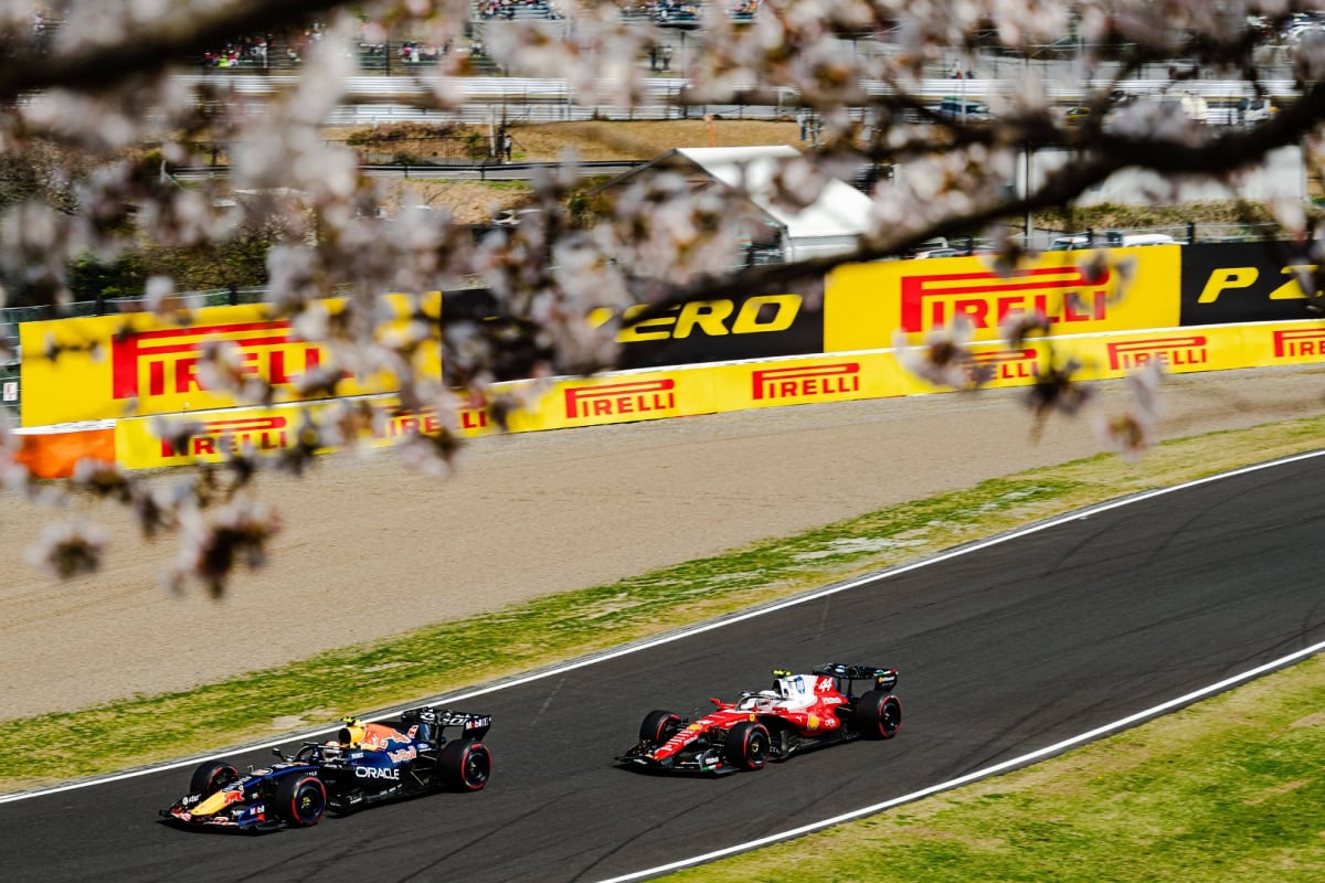 Max Verstappen's Red Bull followed by Lewis Hamilton's Ferrari on track at Suzuka framed by cherry blossom
