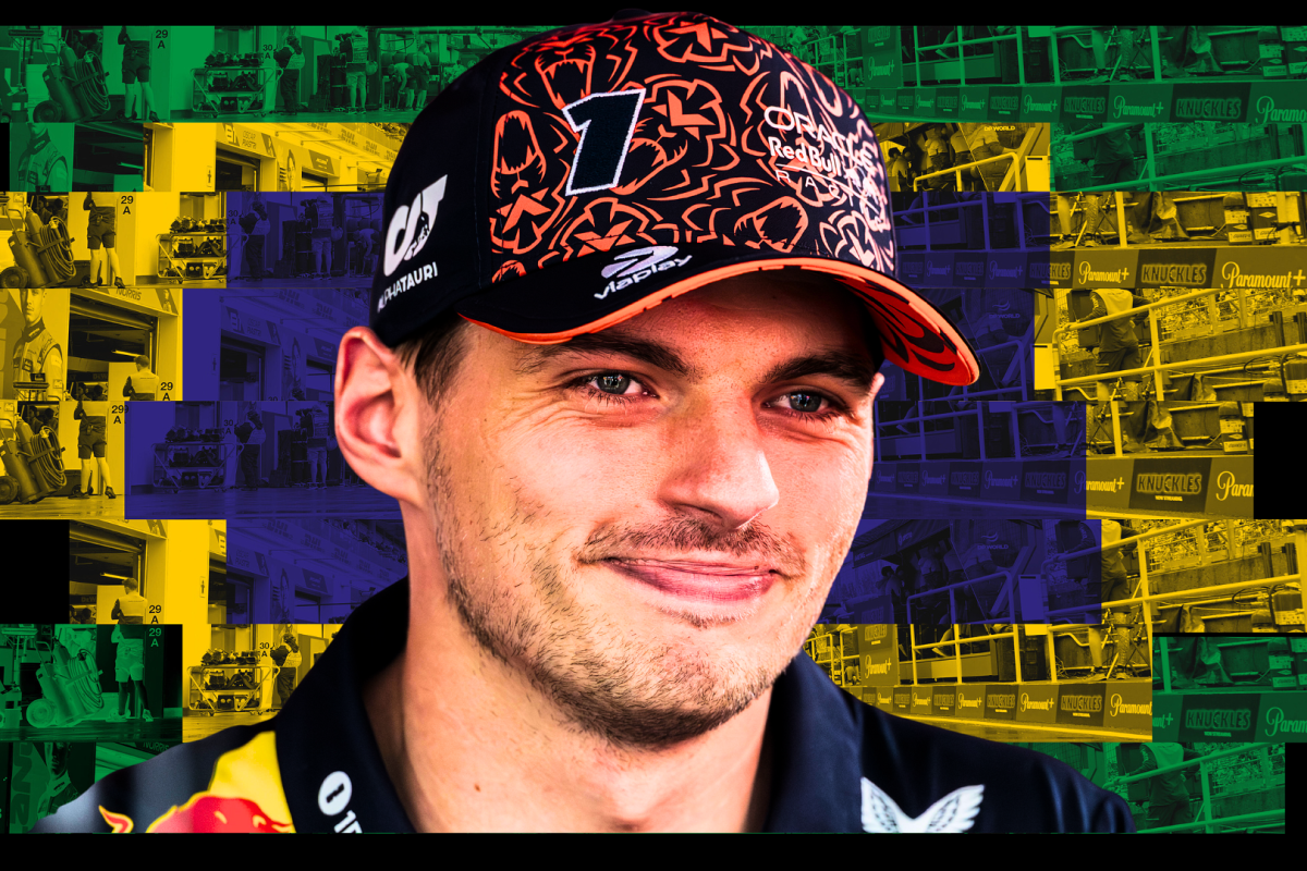 Smiling Max Verstappen in Red Bull team kit with a Brazilian-flag themed paddock background