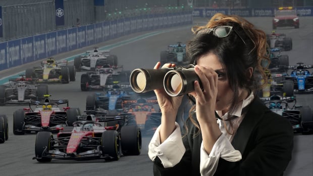 A woman looks through a pair of binoculars to the background of F1 cars — Photo: © IMAGO