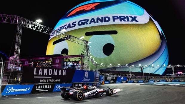 Ollie Bearman driving a Haas F1 car on the Vegas circuit beneath the smiling vegas GP helmet sphere
