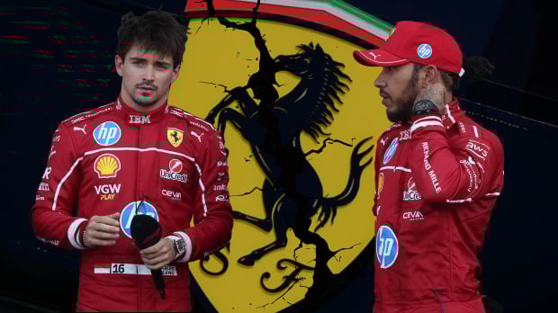 Charles Leclerc and Lewis Hamilton stand in front of an edited cracked Ferrari badge