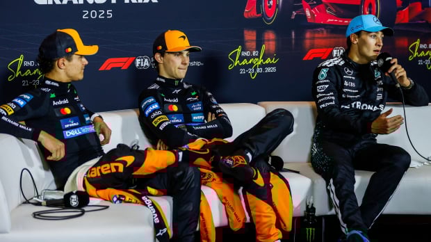 Norris and Piastri looking annoyed at Russell who is holding the F1 mic on the press conference sofa
