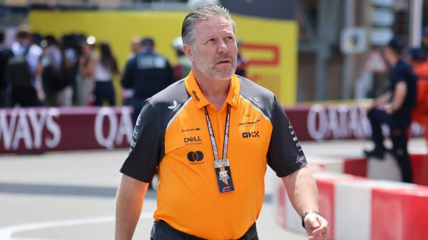 McLaren CEO in papaya McLaren F1 t-shirt and black trousers walking through the F1 paddock with a serious expression