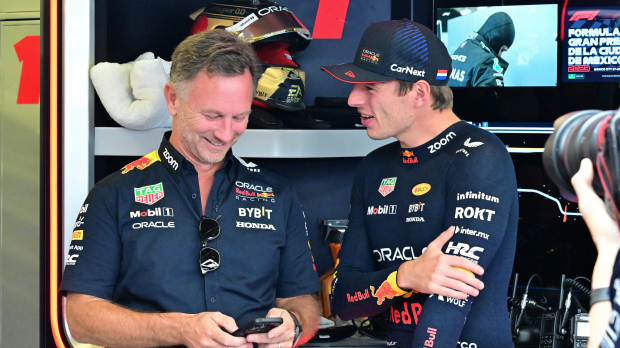 Christian Horner laughs while looking at his phone, while Max Verstappen smiles alongside him
