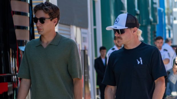 Russell in plain clothes walking through F1 paddock with Bottas in Mercedes hat