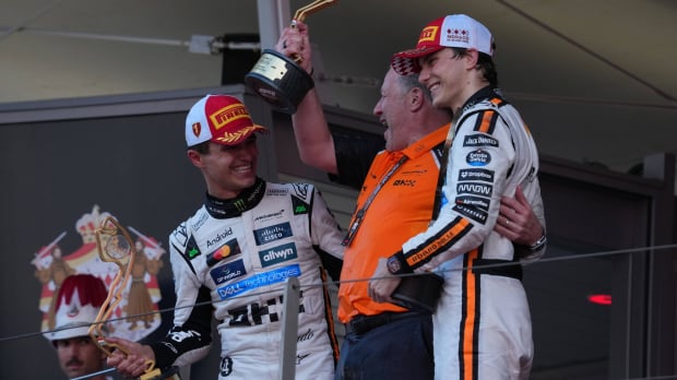 Norris and Brown holding trophies beaming at one another with Piastri joining them on the podium, smiling