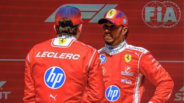 Hamilton facing Leclerc, who has his back to camera, in front of red and white FIA and F1 logo wall — Photo: © IMAGO