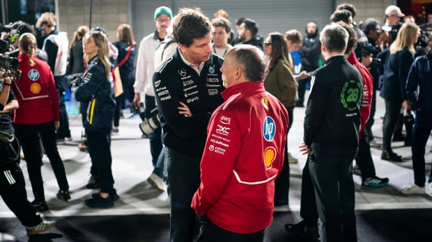 Wolff stood in conversation looking down on Vasseur at F1 track, wearing black Mercedes kit and red Ferrari jacket respectively — Photo: © IMAGO