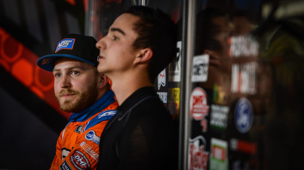 Tyler Courtney looks into the distance wearing a blue hat and orange race suit