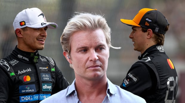 Lando Norris and Oscar Piastri look at one another with a scowling Nico Rosberg between them