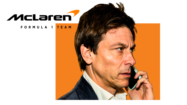 Toto Wolff talks on a phone in front of a McLaren background