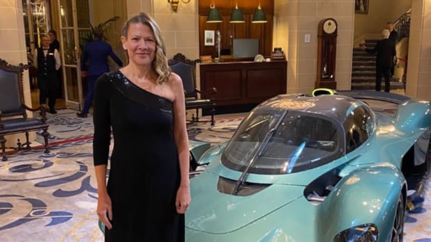 Jennie Gow stands in a black dress in front of turquoise super car — Photo: © @Jennie.Gow