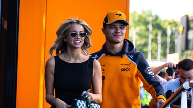 Norris and his girlfriend smiling as they walk into the McLaren motorhome in an F1 paddock