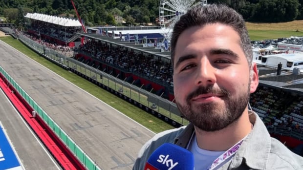 Harry Benjamin taking a selfie with a panoramic view of Imola and holding a Sky Sports microphone 