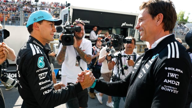 Russell shaking hands with Mercedes boss Wolff at F1 track, both smiling