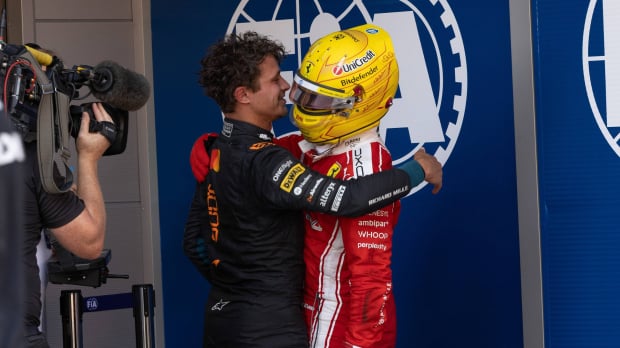 Norris and Hamilton hugging after Barcelona GP in race suits with blue wall in background with white FIA logo on it — Photo: © IMAGO