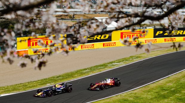 Max Verstappen's Red Bull followed by Lewis Hamilton's Ferrari on track at Suzuka framed by cherry blossom — Photo: © IMAGO