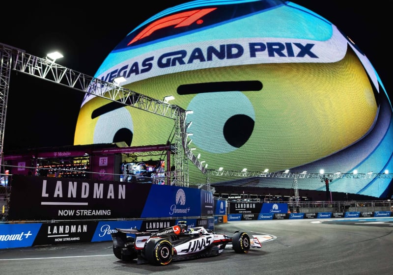 Ollie Bearman driving a Haas F1 car on the Vegas circuit beneath the smiling vegas GP helmet sphere