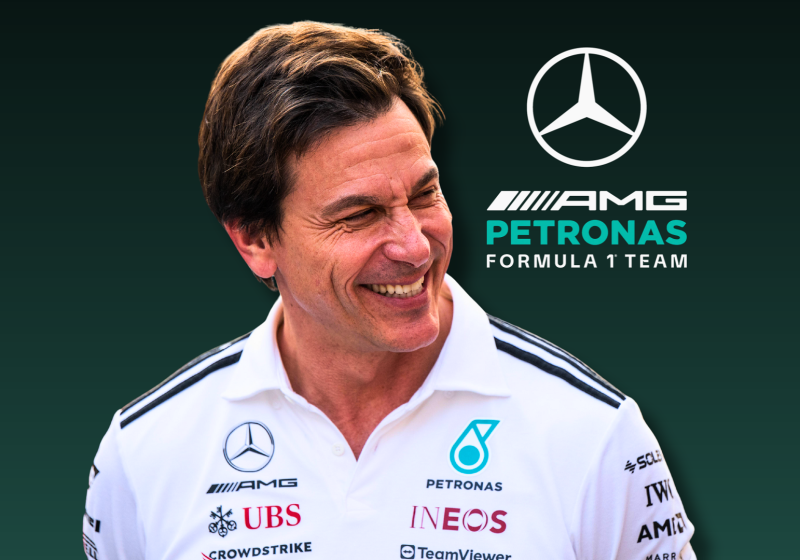 Wolff smiling in white Mercedes shirt with blue and black gradient background featuring F1 logo