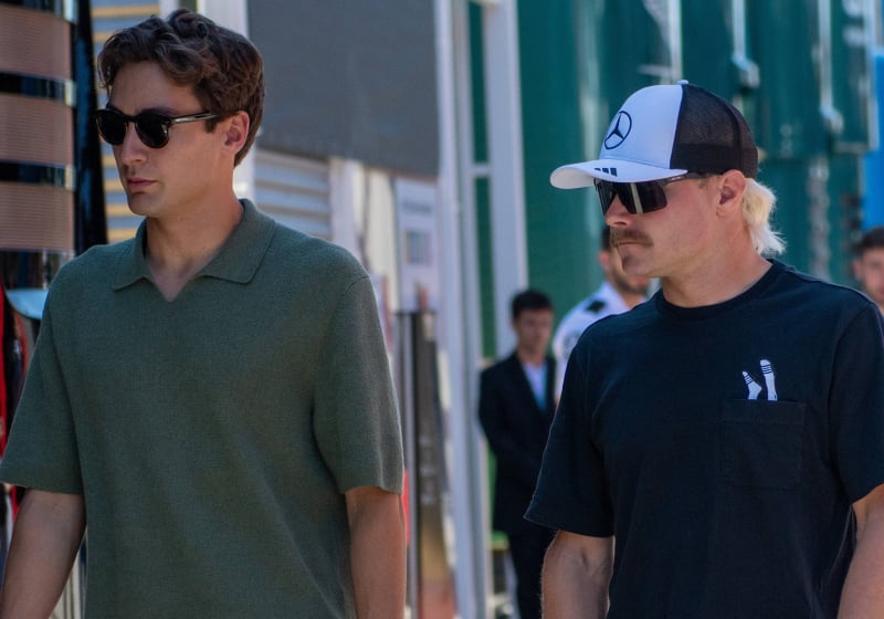 Russell in plain clothes walking through F1 paddock with Bottas in Mercedes hat