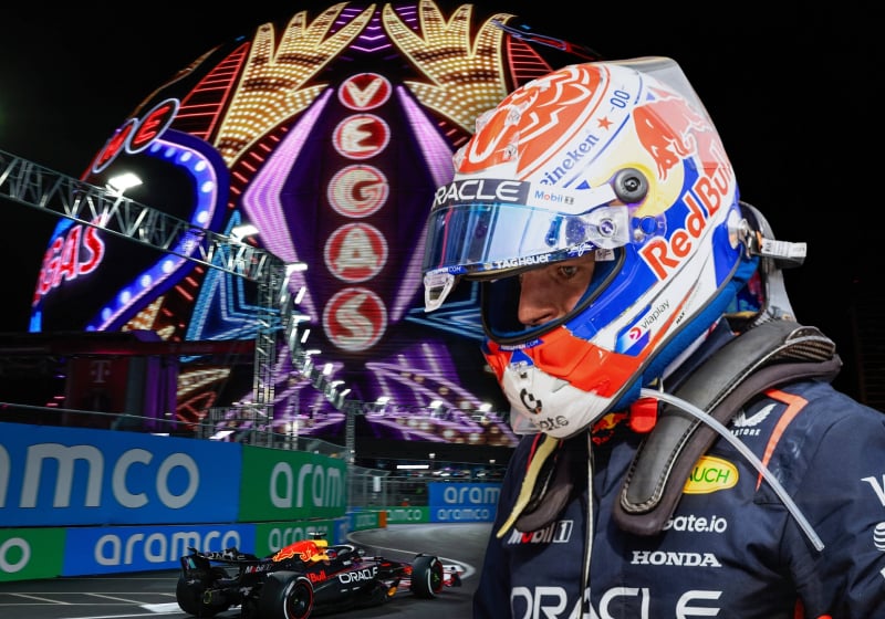 Verstappen in his race suit and helmet edited in front of a picture of a Red Bull car on the Vegas track below the sphere at night