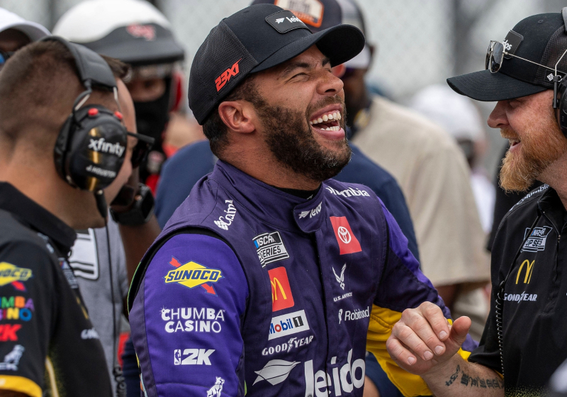 An image of NASCAR driver Bubba Wallace smiling with his 23XI team